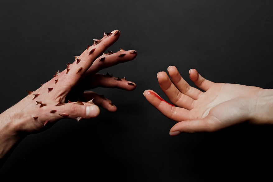 One hand with attached thorns in hurting the other. Gender-based violence concept.